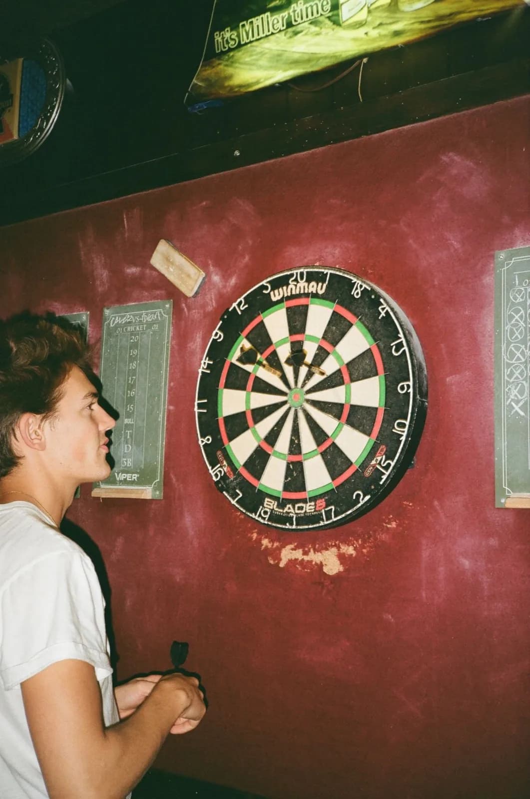 Joueur de fléchettes concentré dans un bar à la peinture bordeaux, photo argentique