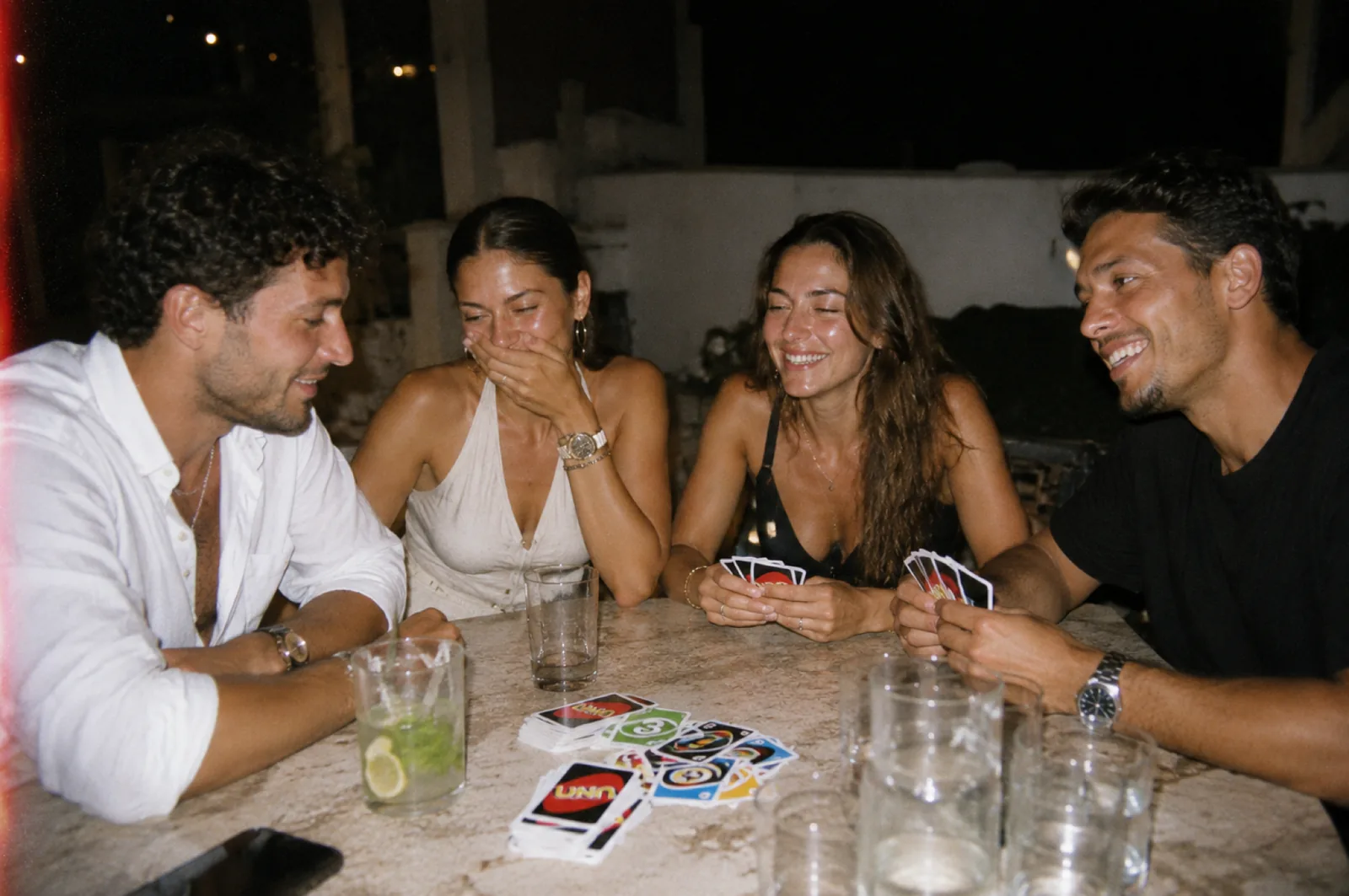 Quatre amis jouant au UNO sur une table en marbre la nuit, fous rires