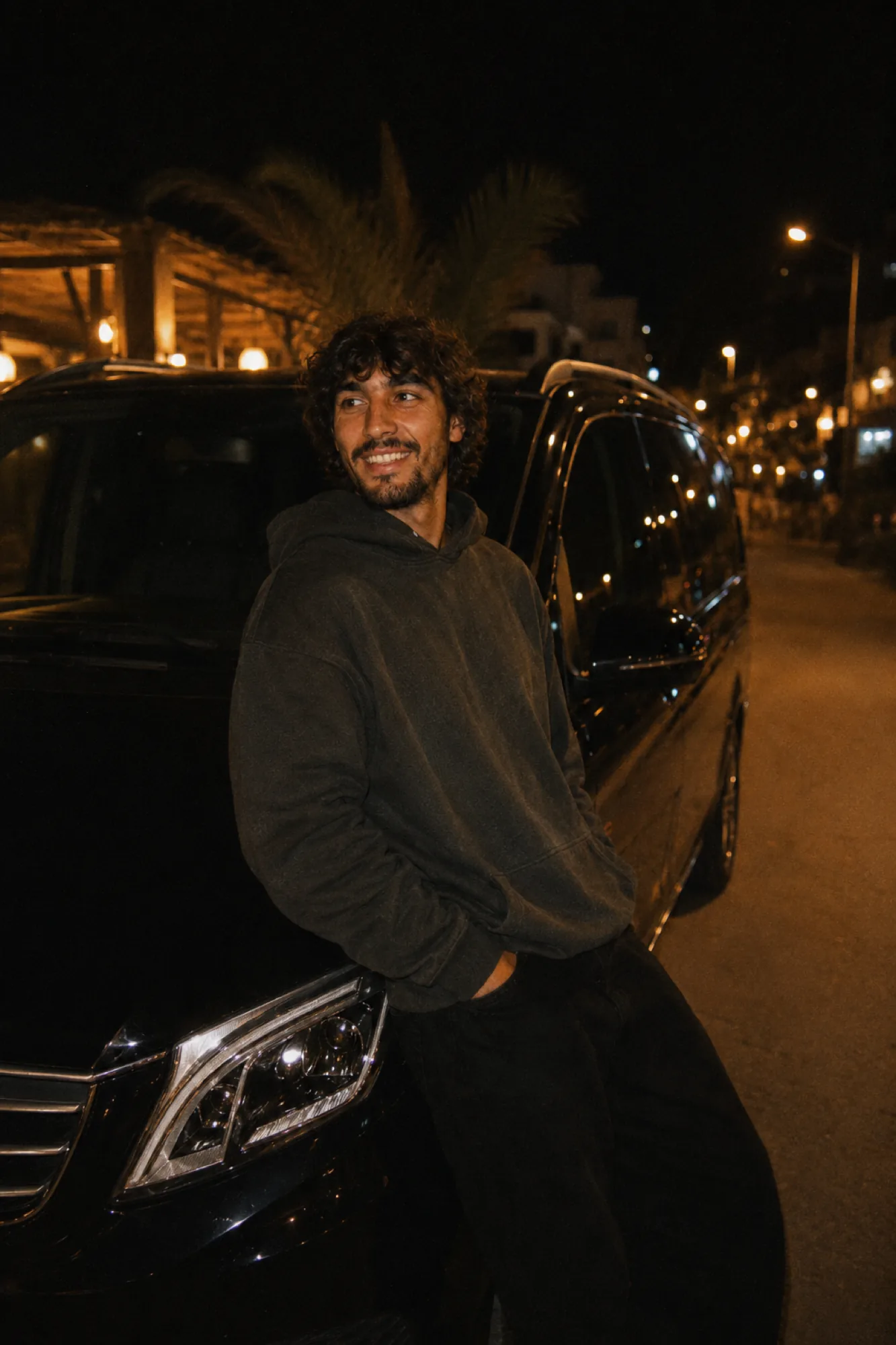Rachid, chauffeur SDM, adossé à son Mercedes Viano noir sous les palmiers la nuit