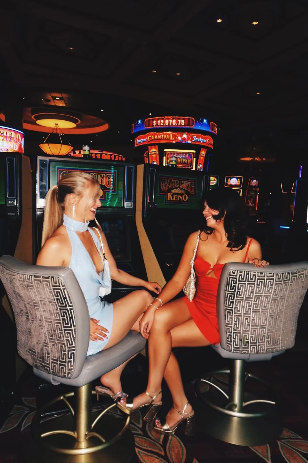 Deux amies en robes de soirée, hilares face à face devant les machines d'un casino