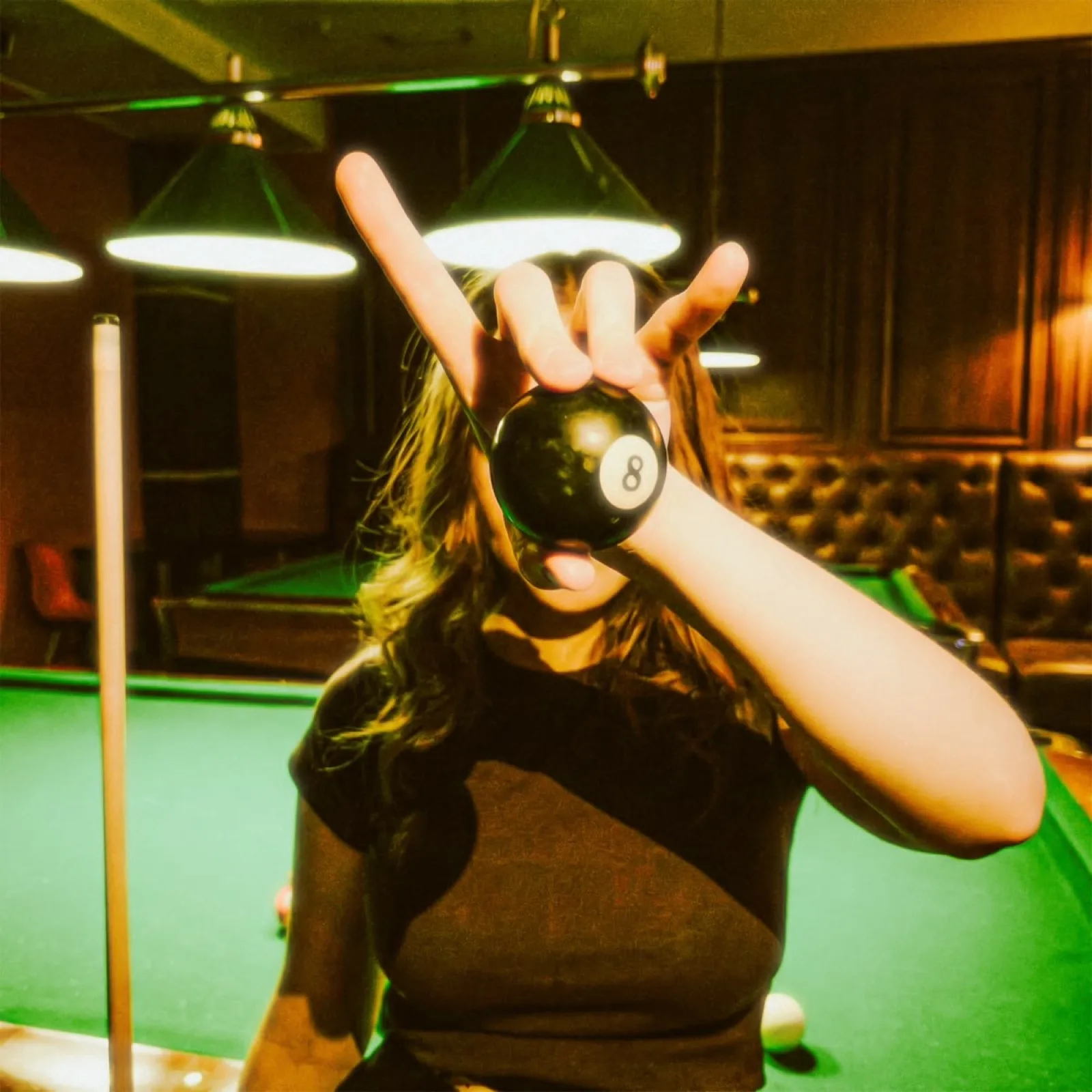 Une joueuse brandit la boule noire numéro 8 devant l'objectif, salle de billard baignée de vert